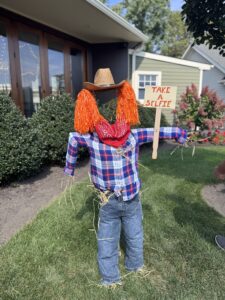 Scarecrow with sign, cowboy hat, and plaid shirt
