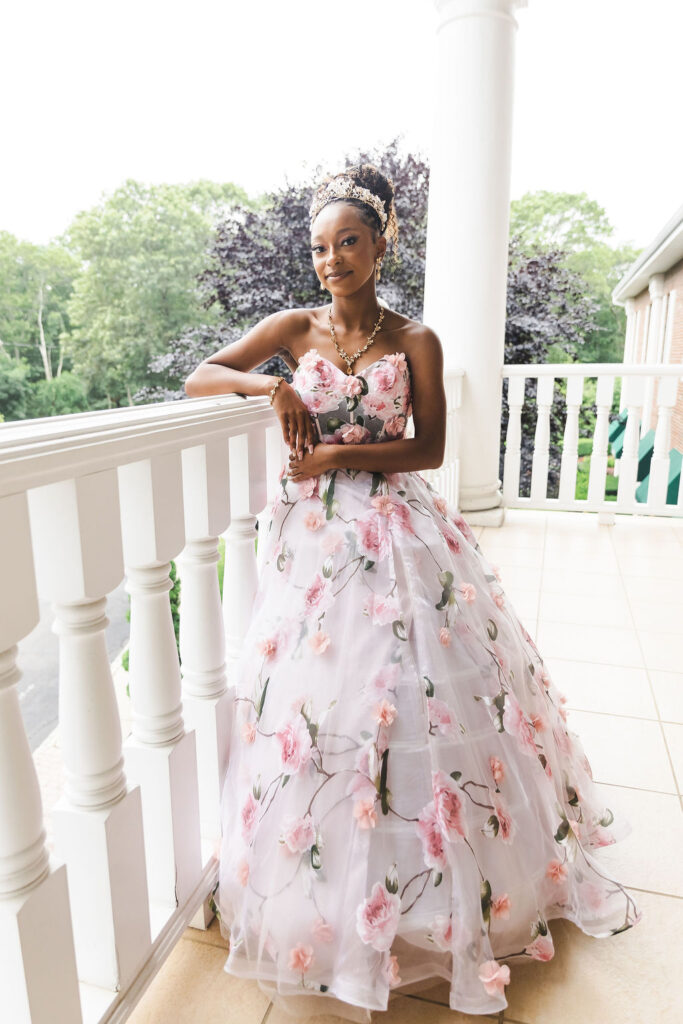 Woman in floral gown on balcony.