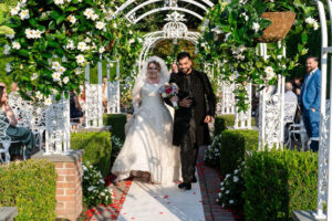 Bride and groom walking in garden aisle.