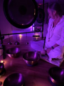 Woman meditating with sound bowls in purple light.